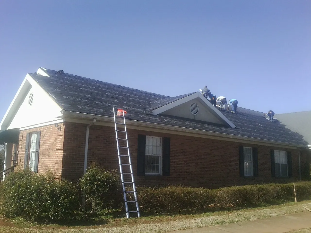 Crew tearing shingles off a brick ranch roof with a ladder set — Metal Roof Repair work by our crew in La Porte