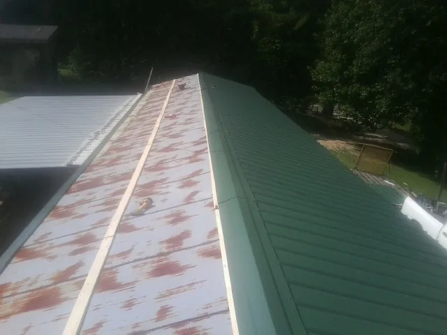 Old rusted panels beside newly installed green metal roofing — Wind Damage Roof Repair by Roofing Brothers in La Porte