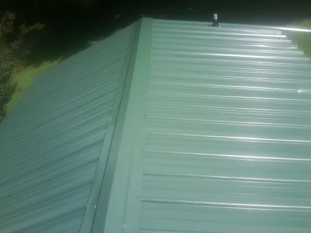 New green metal panels meeting at the ridge of a roof — Flat Roof Repair work by our crew in La Porte