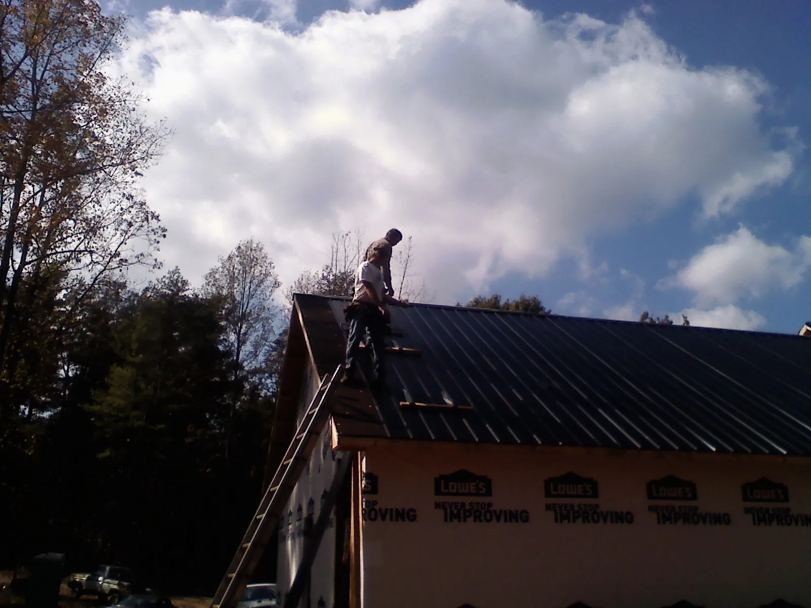 Roofer fastening dark metal panels high against a cloudy sky, from a Roof Inspection job in La Porte
