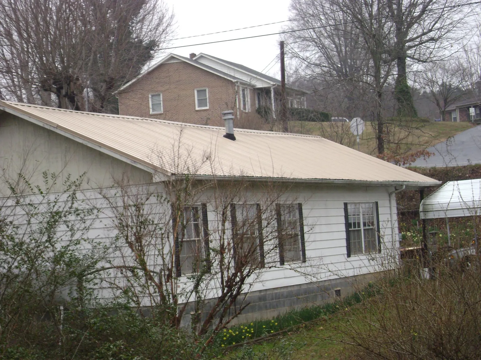 Tan metal roof on a white sided house set into a hillside — Commercial Roofing by Roofing Brothers in La Porte