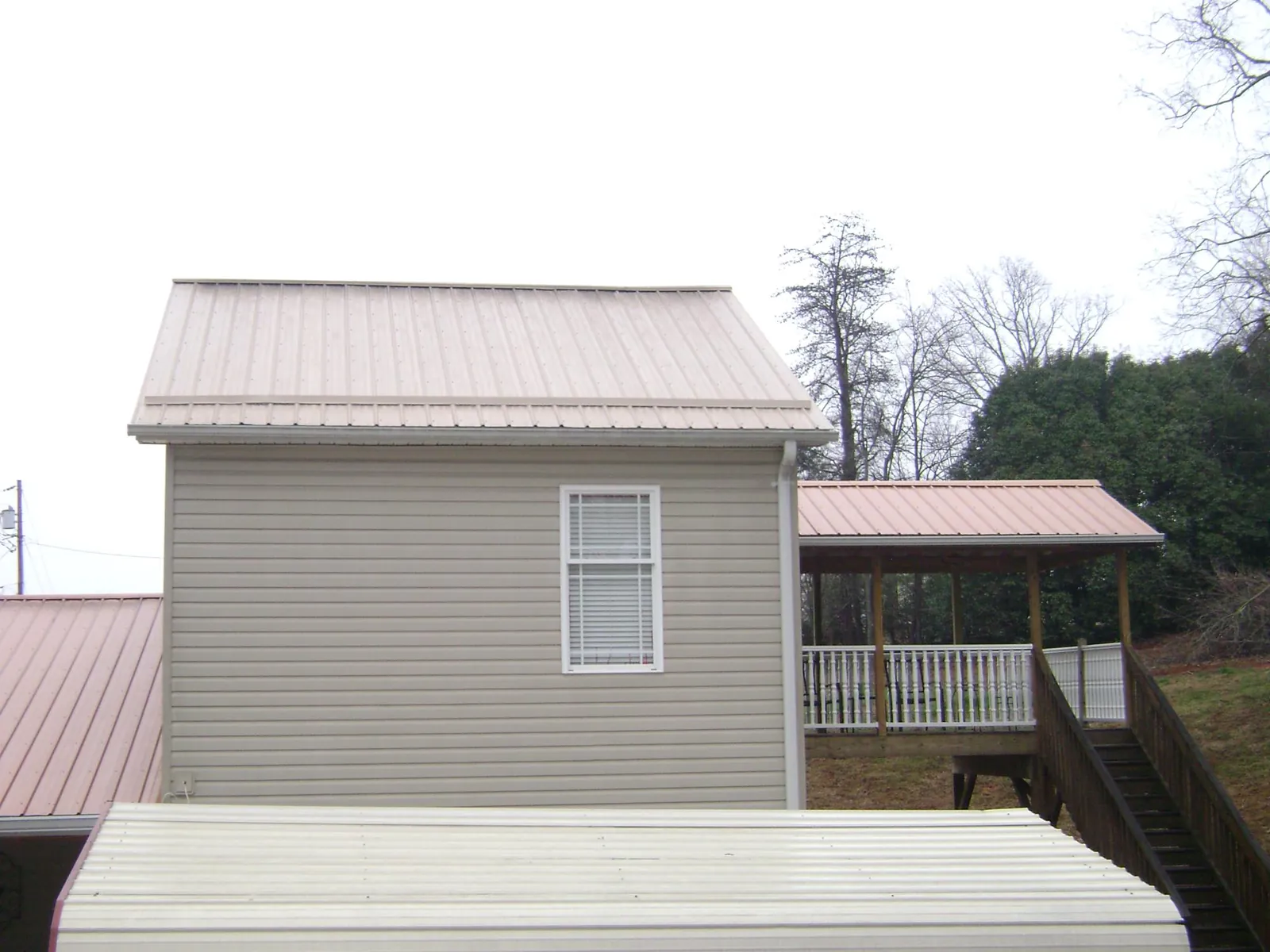 Tan metal roofs on a two story addition and attached porch, from a Roof Replacement job in La Porte